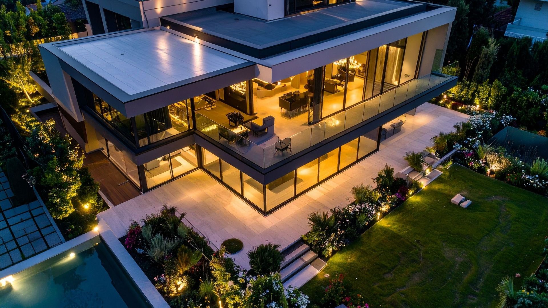 Modern multi-level house with illuminated windows and landscaped garden at night